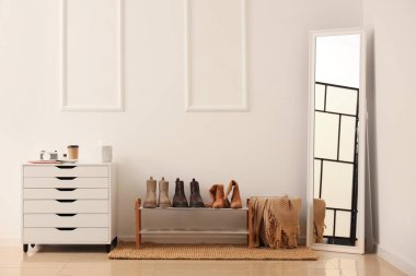 Beyaz duvarın yanında ayakkabı standı, şifonyeri ve aynası olan şık bir koridor.