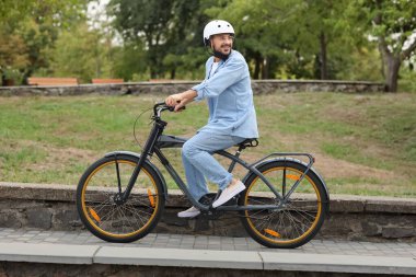 Parkta bisiklet süren kasklı genç adam.