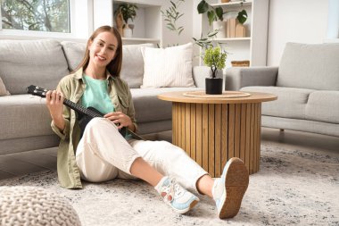 Evdeki halıda ukulele çalan güzel genç bir kadın.