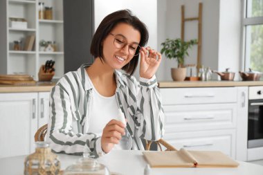 Mutfakta gözlüklü ve göz damlası olan genç bir kadın var.