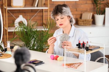 Evde makyaj fırçası ve dekoratif kafa kayıt videosu olan kadın güzellik blogcusu