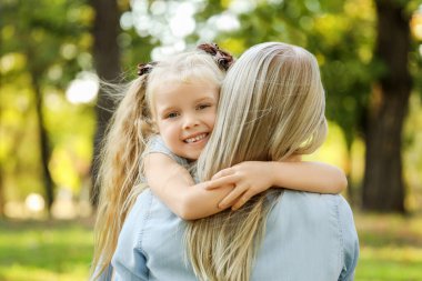 Mutlu anne ve küçük kızı parkta sarılıyorlar, yakın plan.