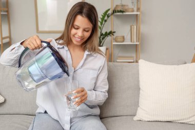 Filtre sürahisinden eve su döken genç bir kadın.