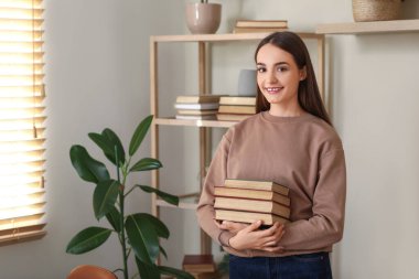 Oturma odasında yığınla kitabı olan genç bir kadın.