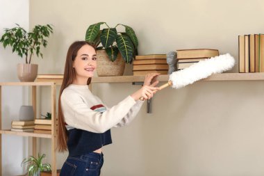 Oturma odasındaki rafları temizleyen genç bir kadın.