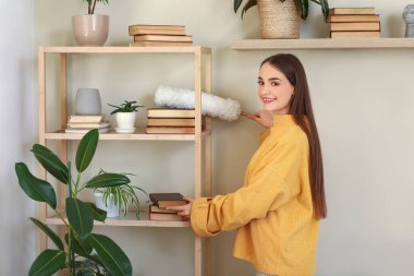 Oturma odasındaki kitap raflarındaki tozları temizleyen genç kadın.