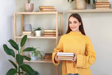 Oturma odasında yığınla kitabı olan genç bir kadın.