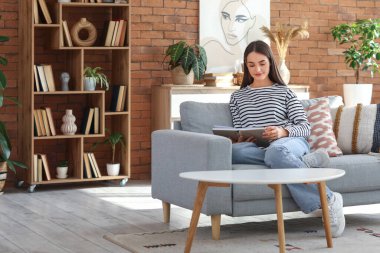 Young woman sitting on sofa and reading book in living room