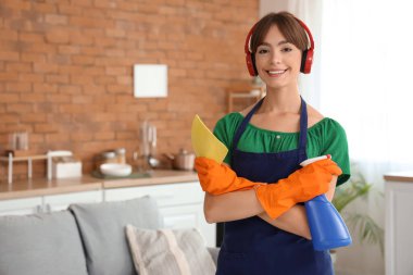 Evde kulaklıkları ve temizlik malzemeleriyle güzel bir bayan var.