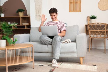 Genç adam evdeki kanepede dizüstü bilgisayarla görüntülü sohbet ediyor.