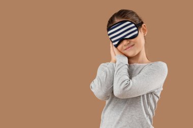 Maskeli, bej arka planda uyuyan pijamalı tatlı küçük bir kız.