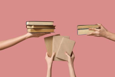 Pembe arka planda bir sürü kitap tutan eller