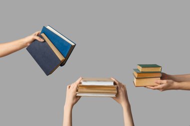 Gri arka planda birçok kitabı tutan eller