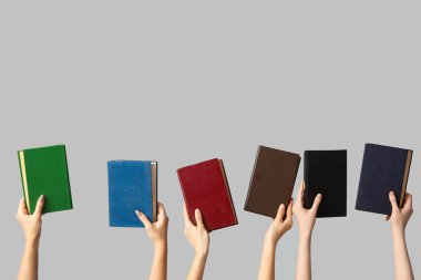 Gri arka planda birçok kitabı tutan eller