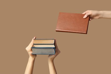 Bej arkaplan üzerine birçok kitap tutan eller