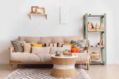 Konforlu kanepe, sehpa ve salonun içinde sonbahar dekoru olan raf ünitesi.