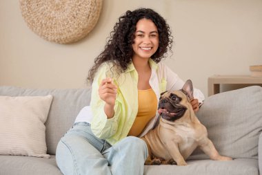 Evdeki kanepede oturan sevimli Fransız bulldoguyla güzel bir Afro-Amerikalı kadın.