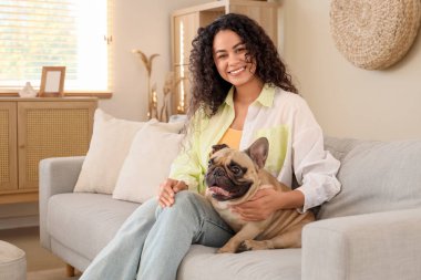 Güzel, genç, Afro-Amerikan bir kadın ve tatlı bir Fransız bulldog 'u oturma odasında kanepede oturuyor.