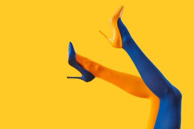 Renkli taytlı genç kadın bacakları ve sarı arka planda yüksek topuklu ayakkabı.