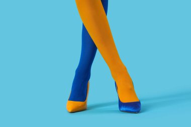 Renkli taytlı genç kadın bacakları ve mavi arka planda yüksek topuklu ayakkabı.