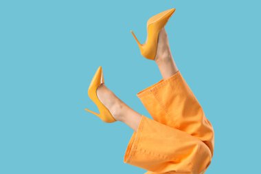 Mavi arka planda sarı topuklu genç kadın bacakları