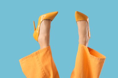 Mavi arka planda sarı topuklu genç kadın bacakları