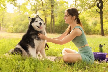 Parktaki çimlerde oturan sevimli Husky köpeği olan genç bir kadın.