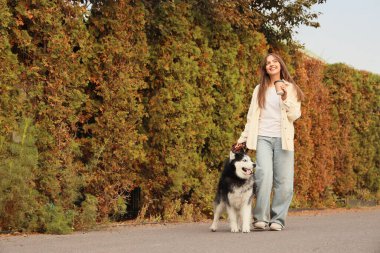 Bir fincan kahve ve parkta yürüyen sevimli Husky köpeğiyle mutlu genç bir kadın.