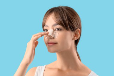 Mavi arka planda sargılı burnu olan güzel, genç bir kadın. Estetik ameliyat konsepti