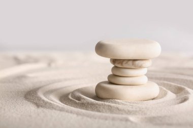 Gri arkaplandaki çizgilerle aydınlık kumda taş yığını. Zen kavramı