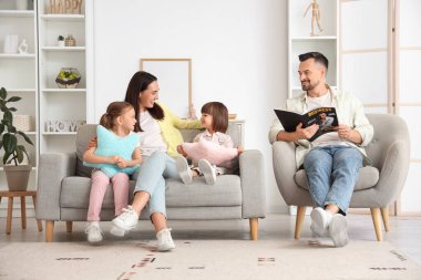 Babaları evdeki koltukta dergi okurken anneleri kızlarıyla mutlu.