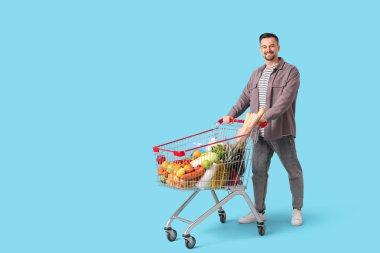 Mavi arka planda alışveriş arabası olan mutlu genç bir adam.