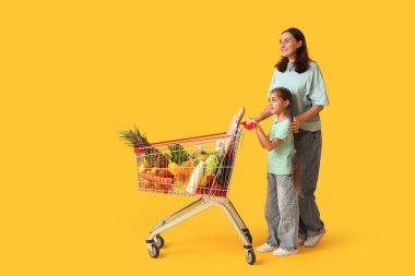 Güzel, genç, mutlu anne ve kızı sarı arka planda alışveriş arabalarıyla.