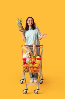 Güzel, genç, mutlu bir kadın alışveriş arabası ve sarı arka planda ananas.