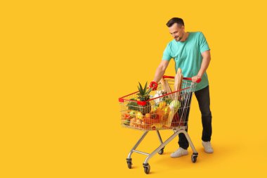 Sarı arka planda alışveriş arabası olan mutlu genç bir adam.