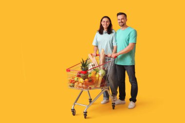 Sarı arka planda alışveriş arabası olan genç ve güzel bir çift.