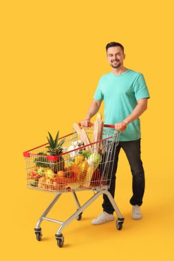Sarı arka planda alışveriş arabası olan mutlu genç bir adam.