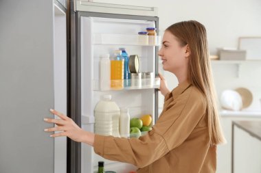 Mutfaktaki açık buzdolabının yanında genç bir kadın.