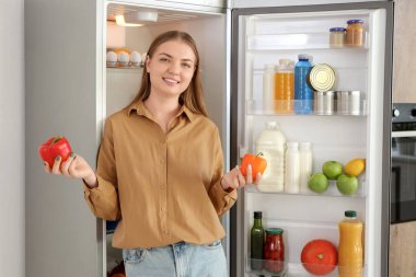 Mutfaktaki açık buzdolabının yanında biberli genç bir kadın.