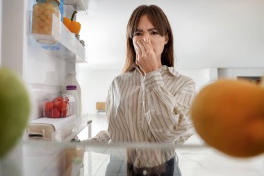 Genç bir kadın mutfaktaki açık buzdolabından kötü bir koku alıyor.