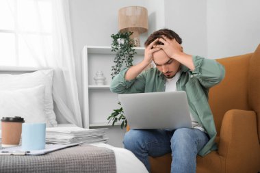 Yatak odasında dizüstü bilgisayarla çalışan stresli genç adam.