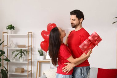 Evde hediye kutusuyla kucaklaşan sevgi dolu bir çift. Sevgililer Günü kutlaması