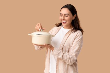Elinde bej arka planda lezzetli çorbayla pişirme kabı tutan genç bir kadın.