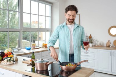 Mutfakta sebze kızartan bir bardak şarapla yakışıklı sakallı adam.