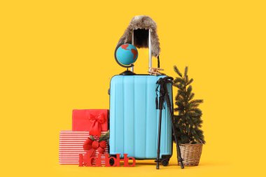 Sarı arka planda Noel ve seyahat aksesuarlarıyla dolu bavul