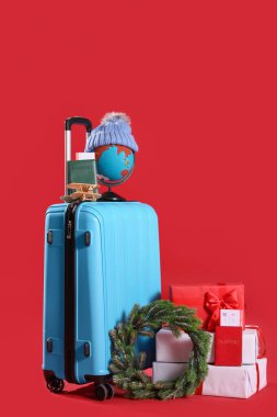 Kırmızı arka planda Noel dekorasyonu ve seyahat aksesuarları olan bavul