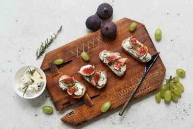 Beyaz arka planda ricotta peyniri ve üzümlü lezzetli incirli bruschetta tahtası.