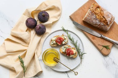 Lezzetli incirli bruschetta tabağı mavi peynirli ve beyaz arka planda bal kasesi.