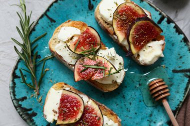 Beyaz arka planda ricotta peynirli ve biberiyeli lezzetli incirli bruschetta tabağı.