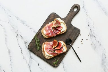 Beyaz arka planda prosciutto ve ricotta peynirli lezzetli incirli bruschetta tahtası.